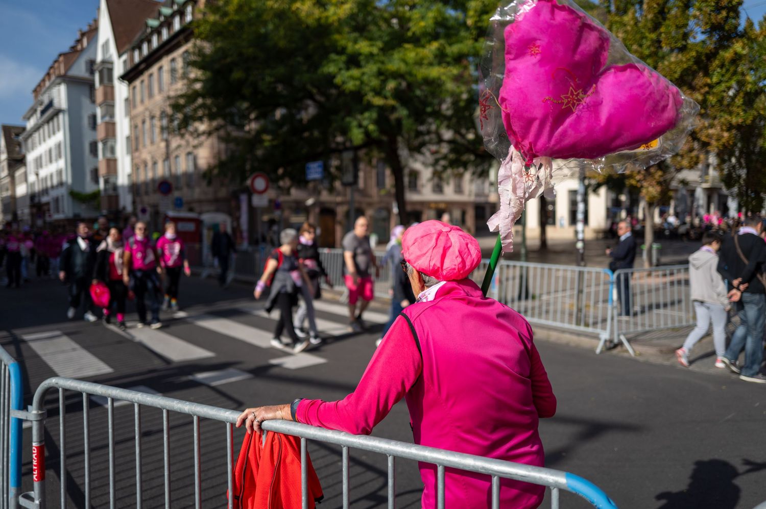 Person in bright pink clothing leaning against barrier during street event.