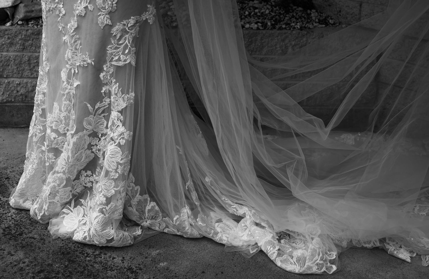 Close-up details of delicate lace wedding dress and flowing veil in black and white.