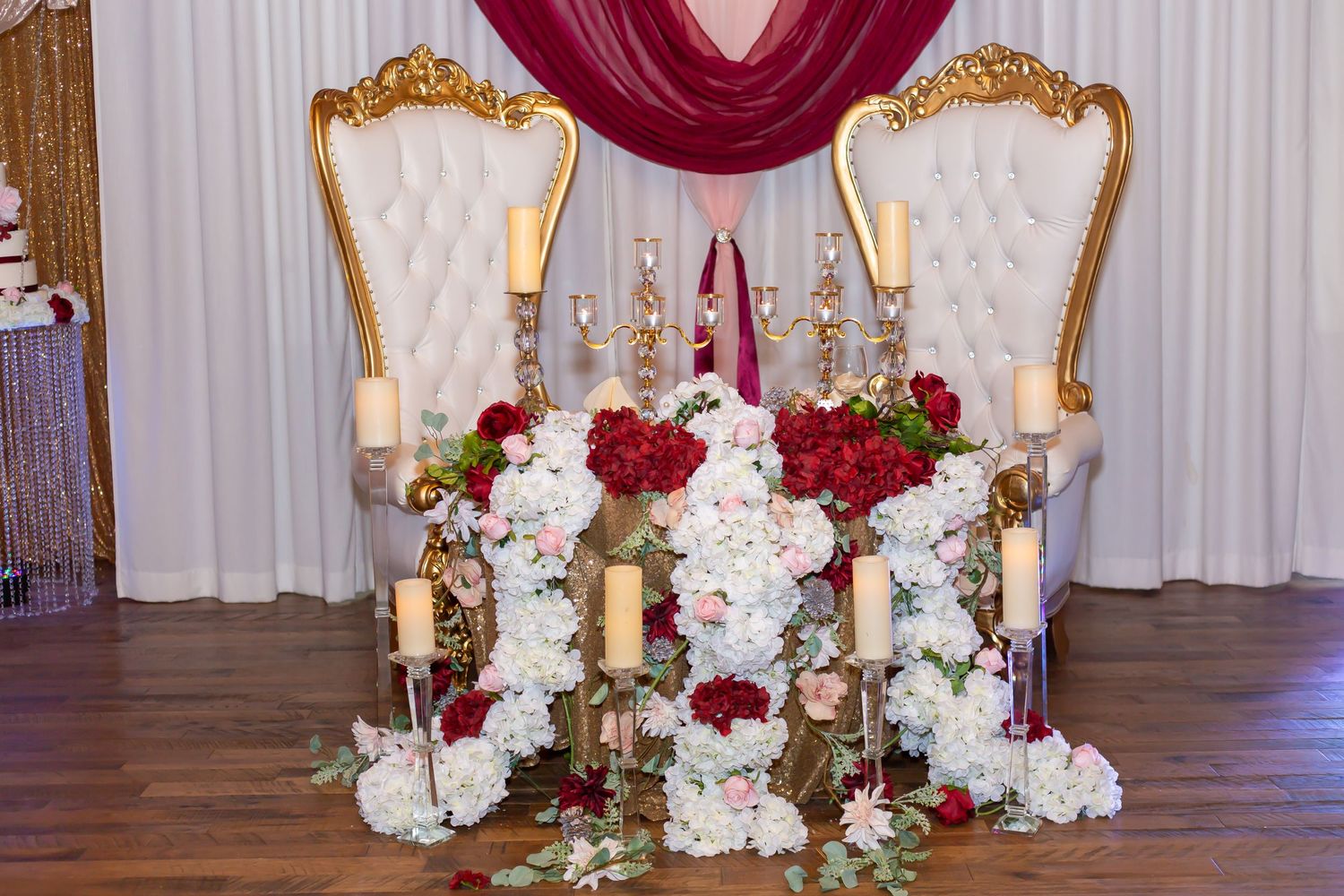 Luxurious throne-style chairs with red and white floral arrangements for a wedding reception.