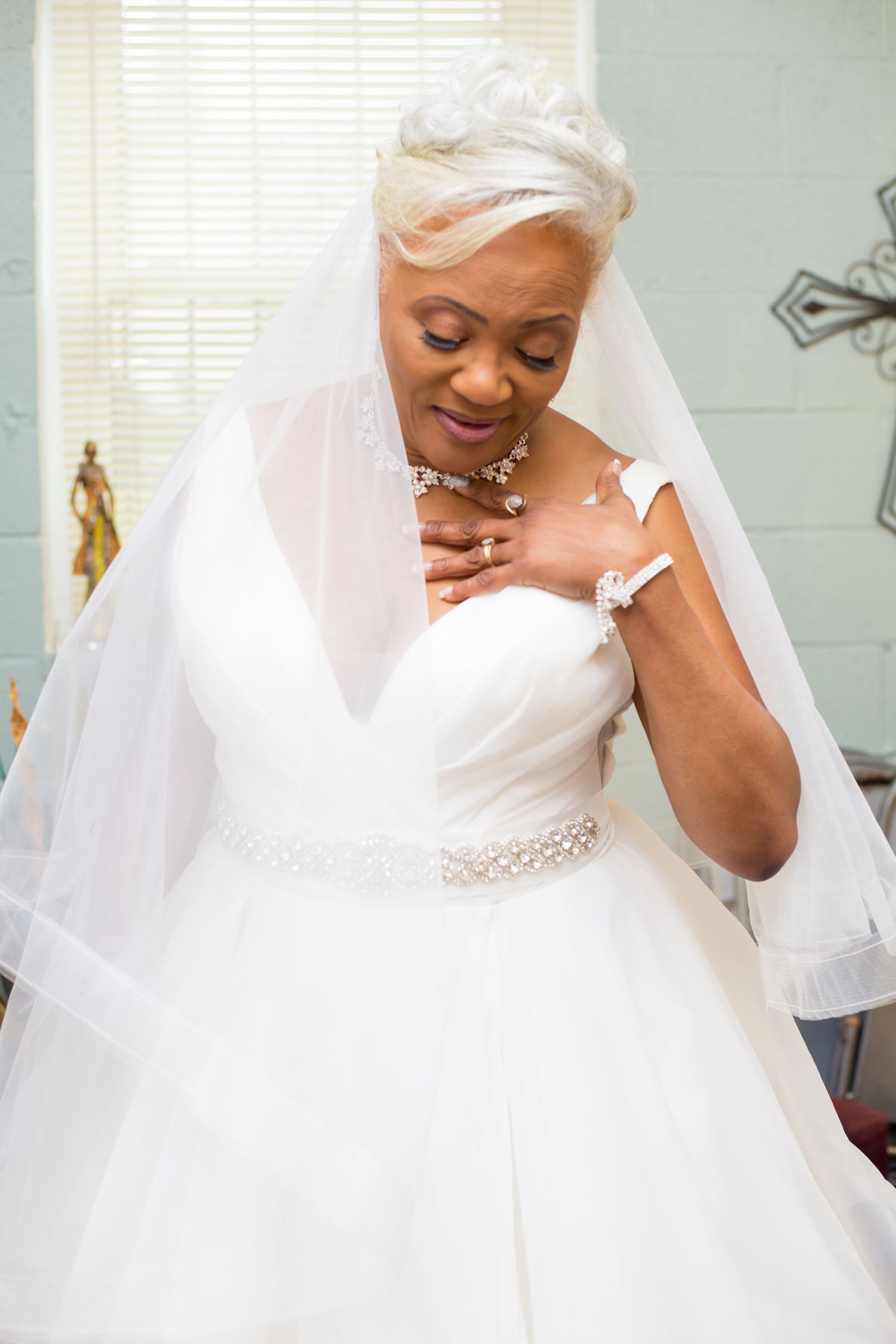A bride in an elegant white ball gown and veil touches her necklace during a tender moment.