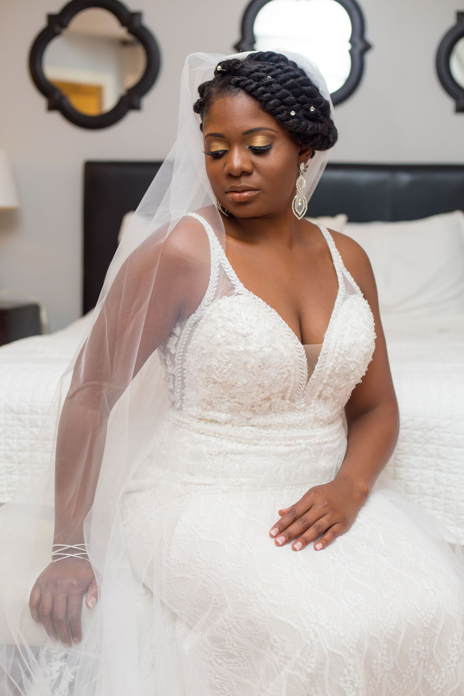 Bride in lace wedding gown sits elegantly with detailed veil and beaded hairstyle.