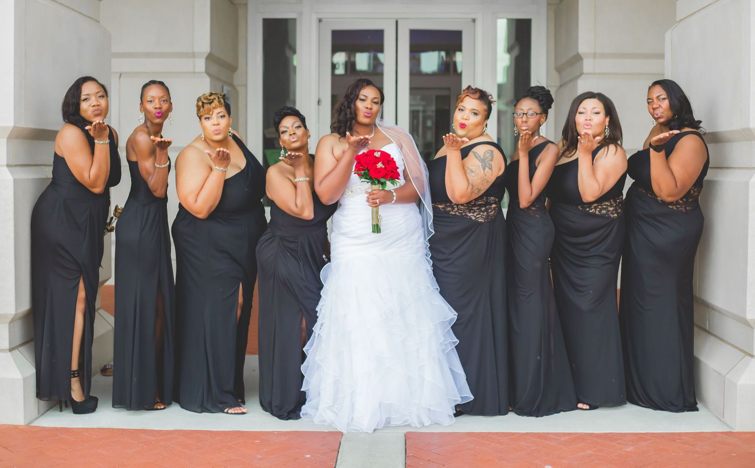 Bridal party in black dresses poses dramatically with bride in white gown.
