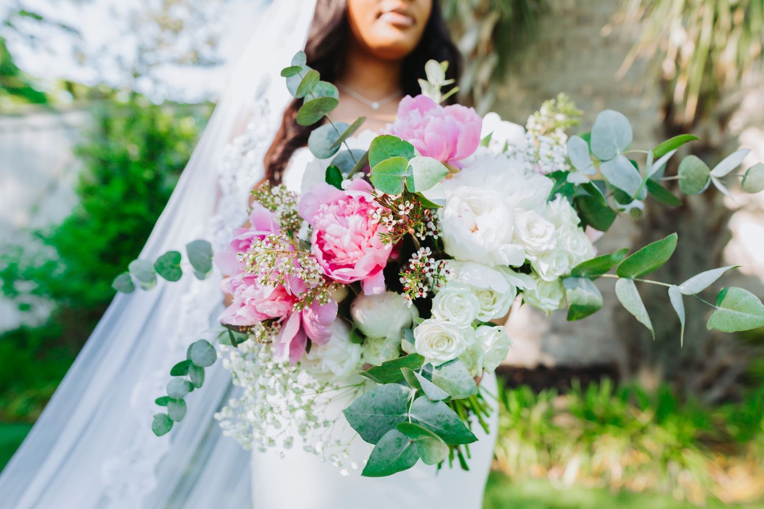 Elegant bridal bouquet with pink and white flowers and eucalyptus leaves against flowing white veil.