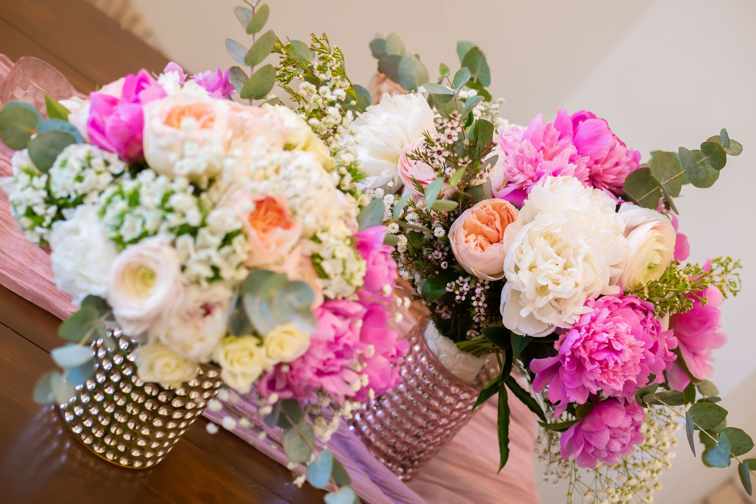 Vibrant wedding bouquets featuring pink and peach flowers with eucalyptus in crystal-adorned vases.