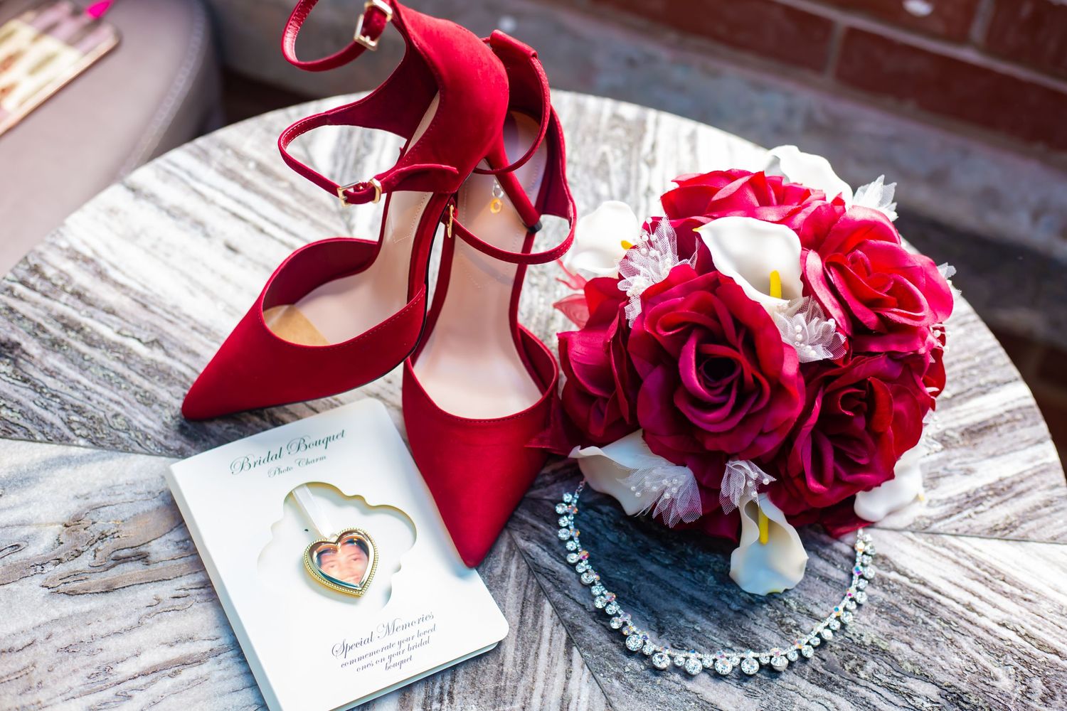 Red bridal shoes next to a bouquet of roses and wedding rings on a textured surface.