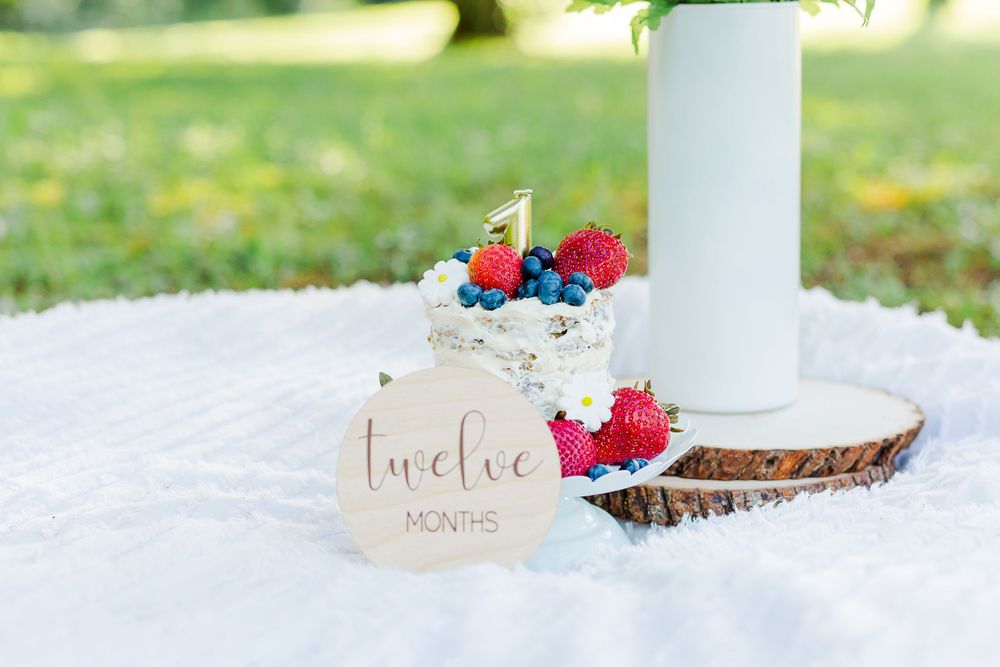 White decorated cake with fresh berries on wooden slice against white blanket outdoors.