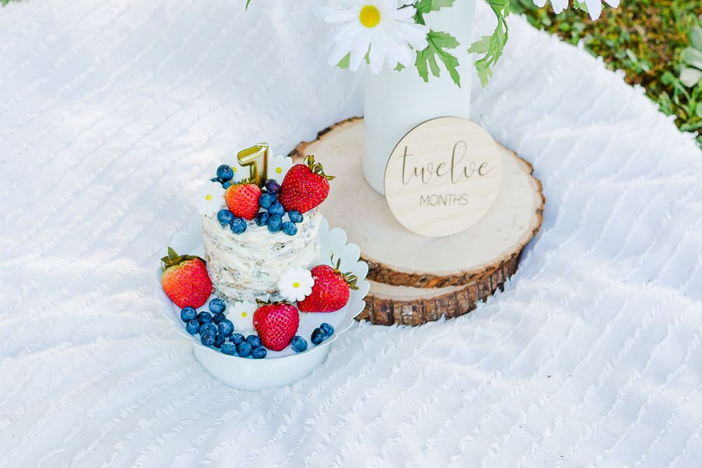First birthday cake topped with fresh strawberries and blueberries on rustic wood slice.
