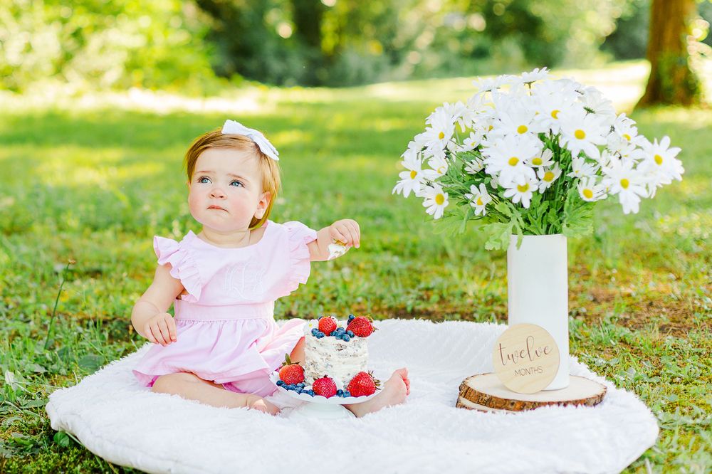 Garden picnic setup with white flowers, berries and cake on blanket.