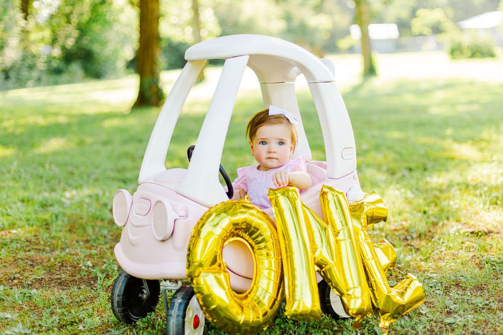 White toy car with gold ONE balloon letters photographed in sunny outdoor setting.