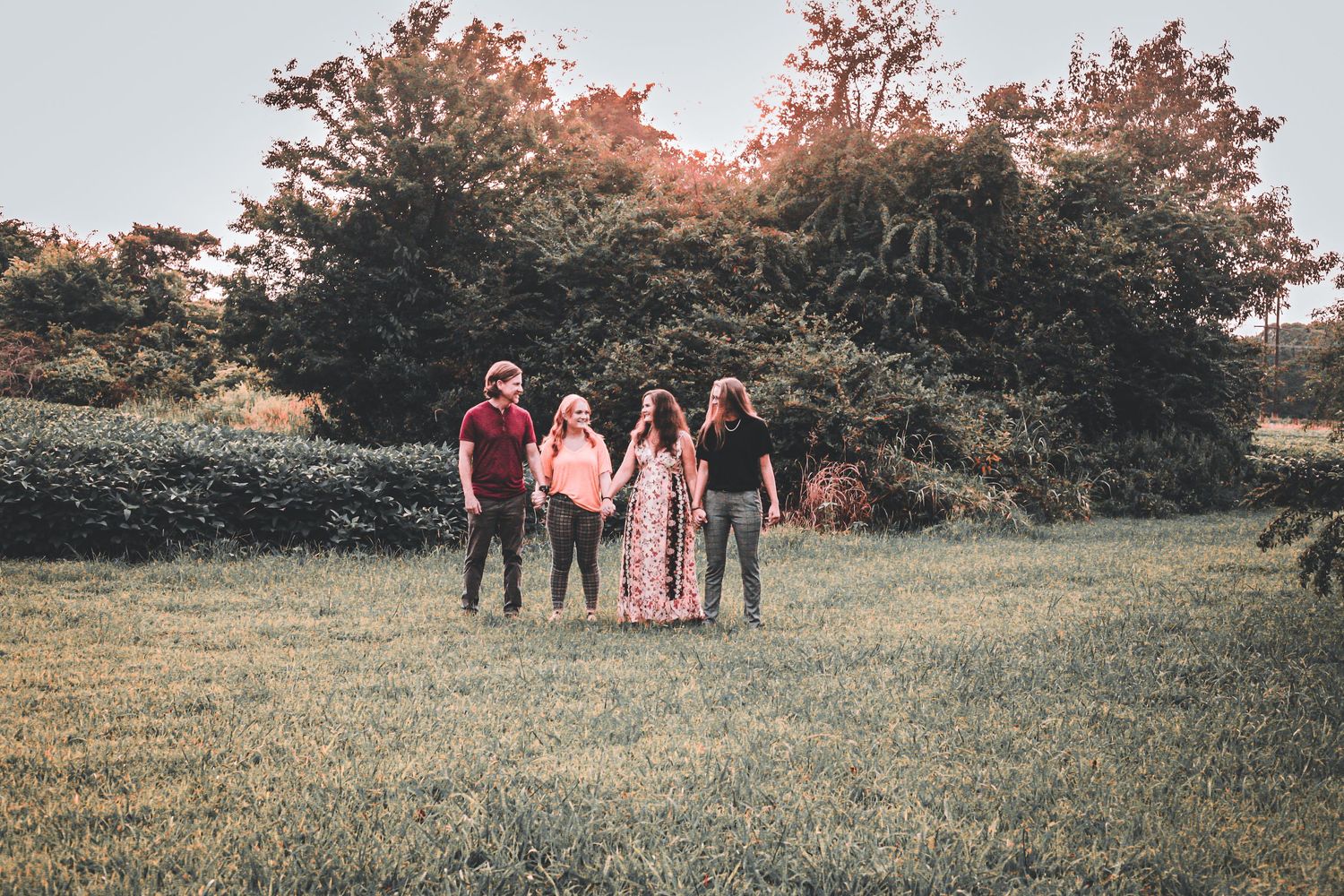 A group walks together across a grassy field at sunset with trees in the background.