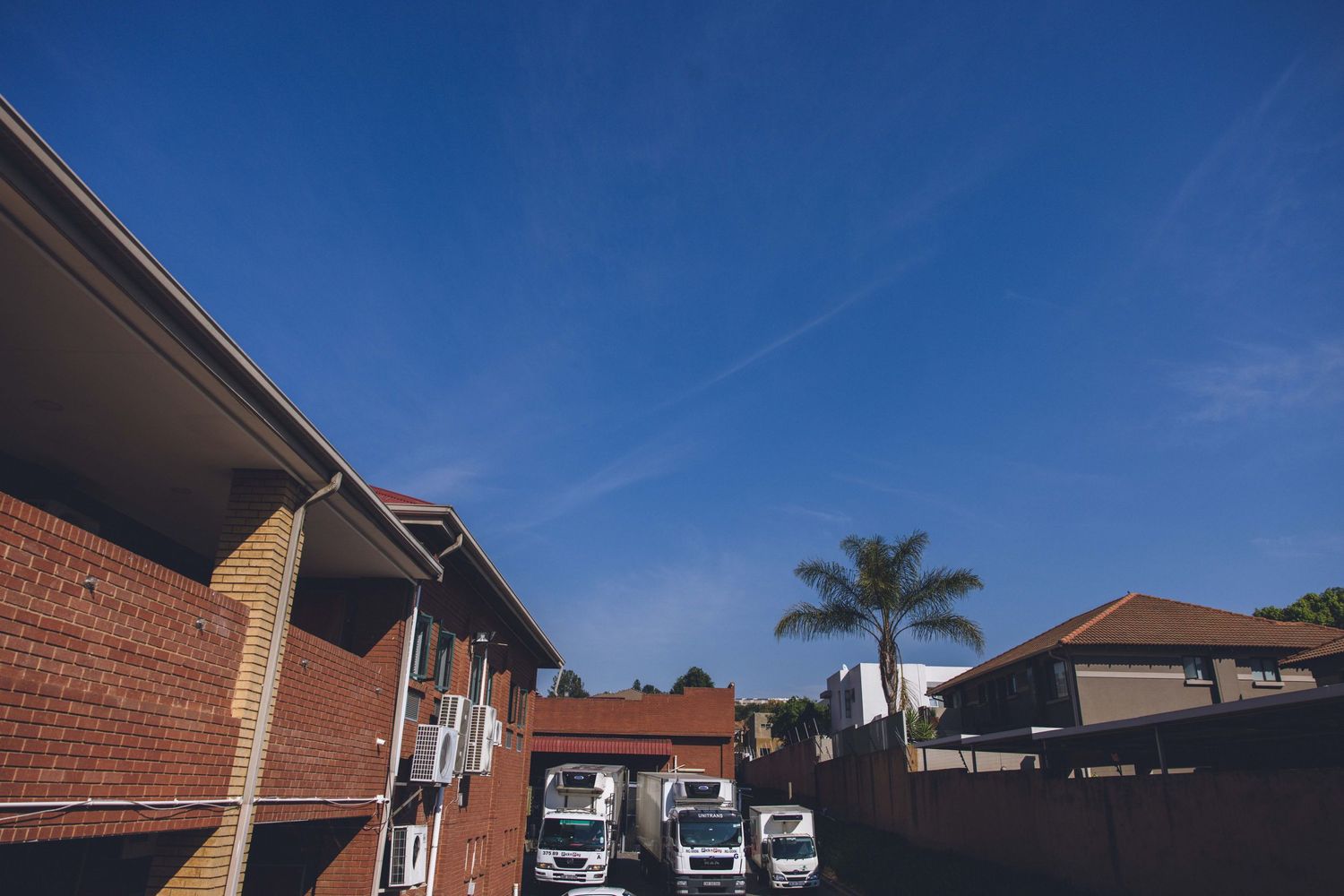 Modern brick building complex with parked vehicles under blue sky.