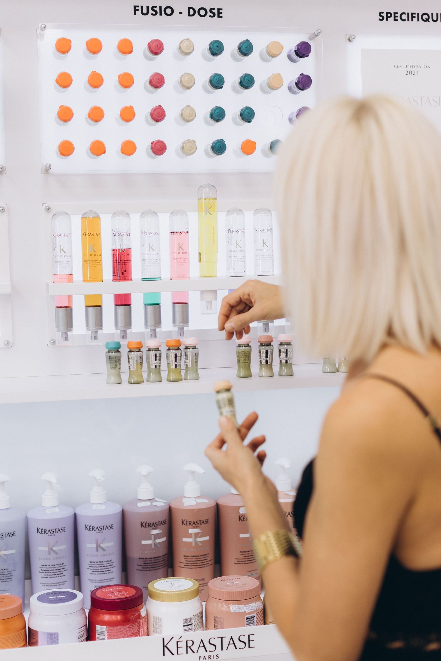 Professional hair products displayed on white shelves with colorful samples and Kerastase bottles.