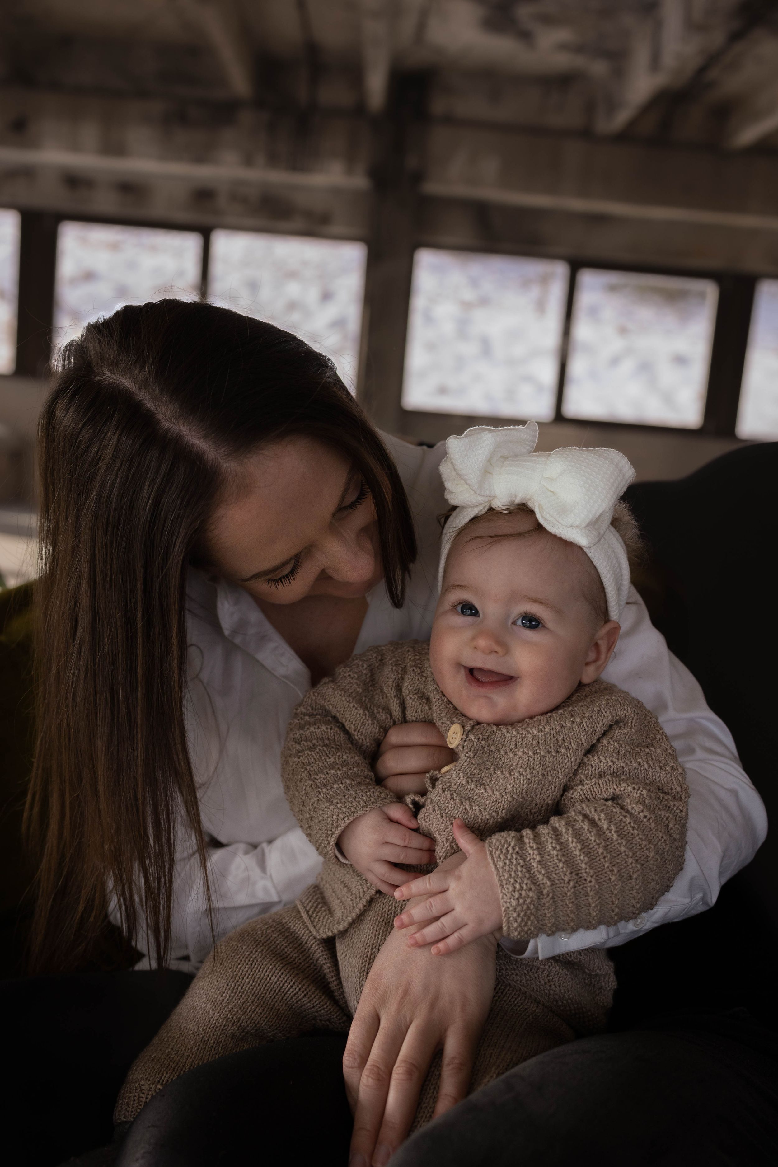 Sweet moment between parent and baby wearing matching beige outfits in industrial space.