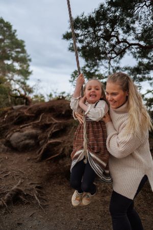Joyful moment of parent helping child on rope swing in forest setting.