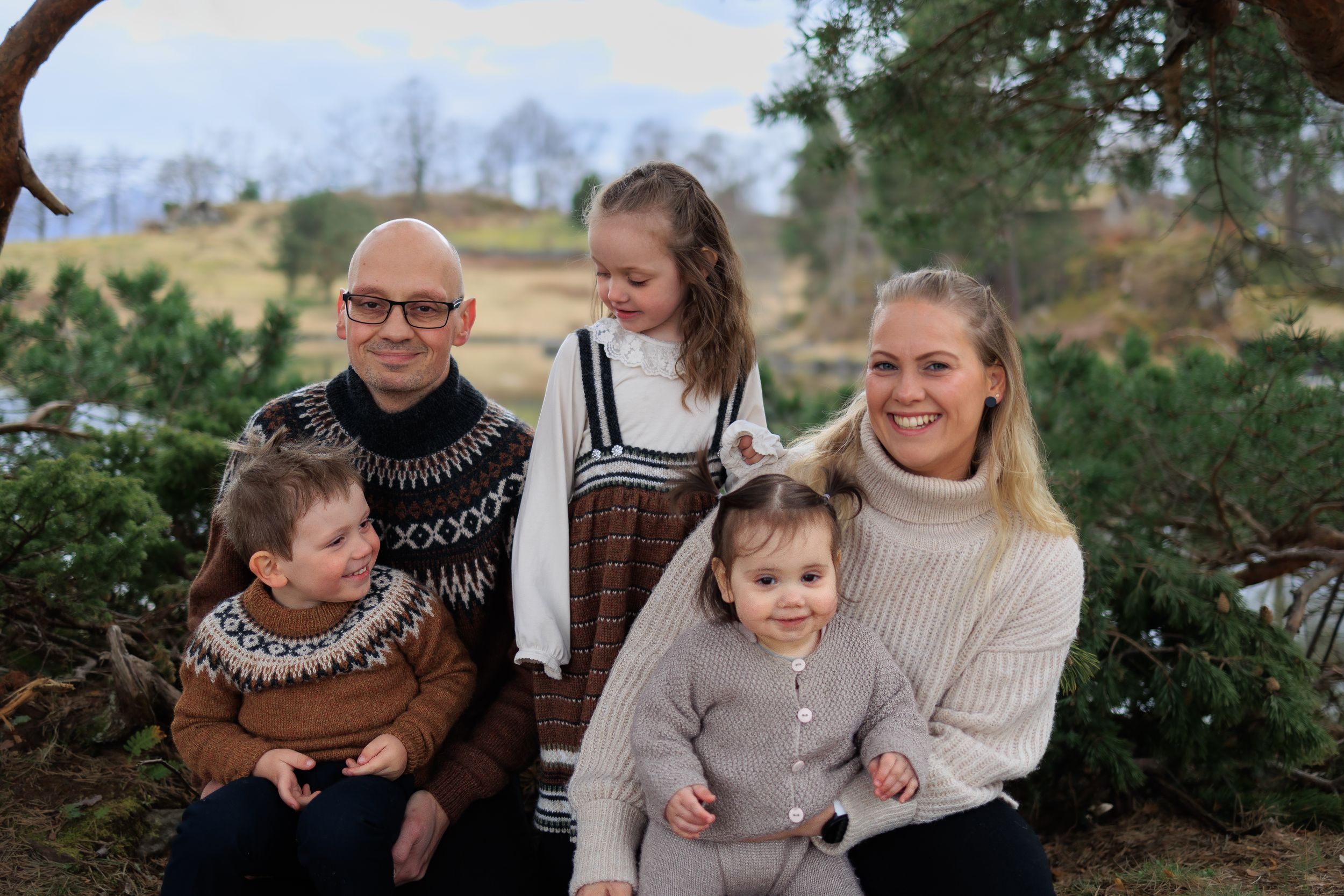 Family portrait with matching Nordic sweaters against natural outdoor setting.