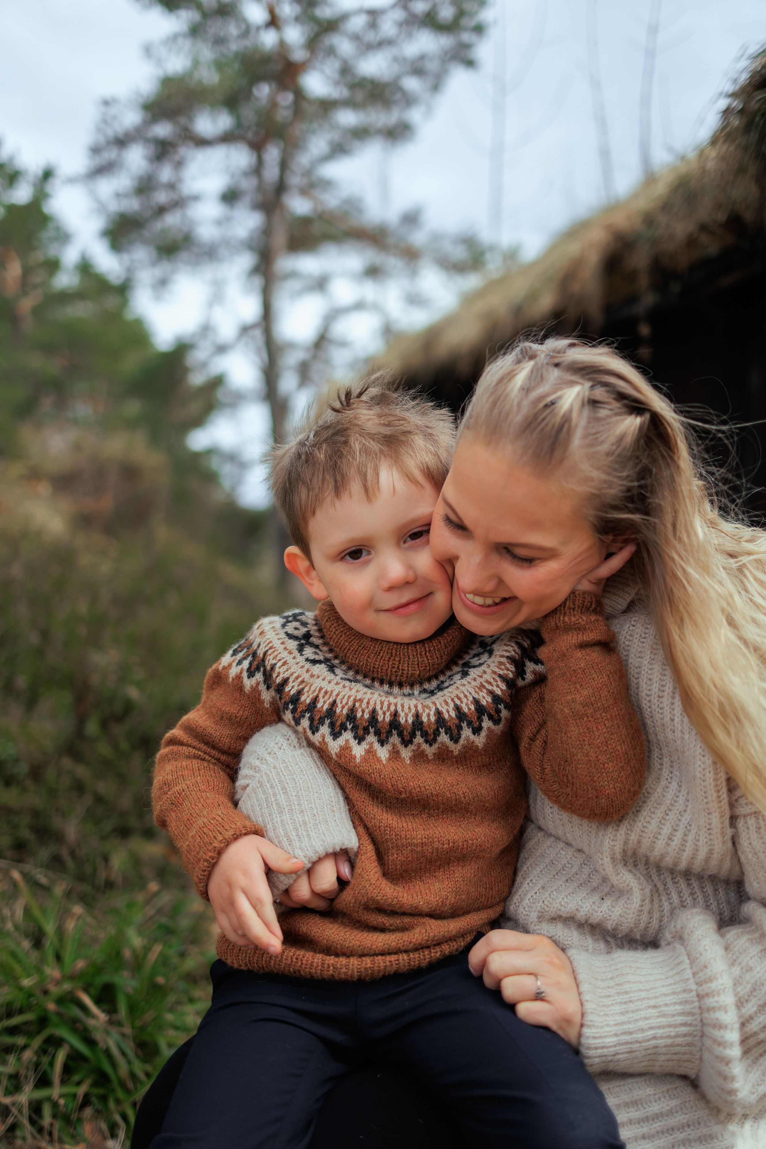 Tender moment between parent and child wearing matching brown Fair Isle sweaters outdoors.