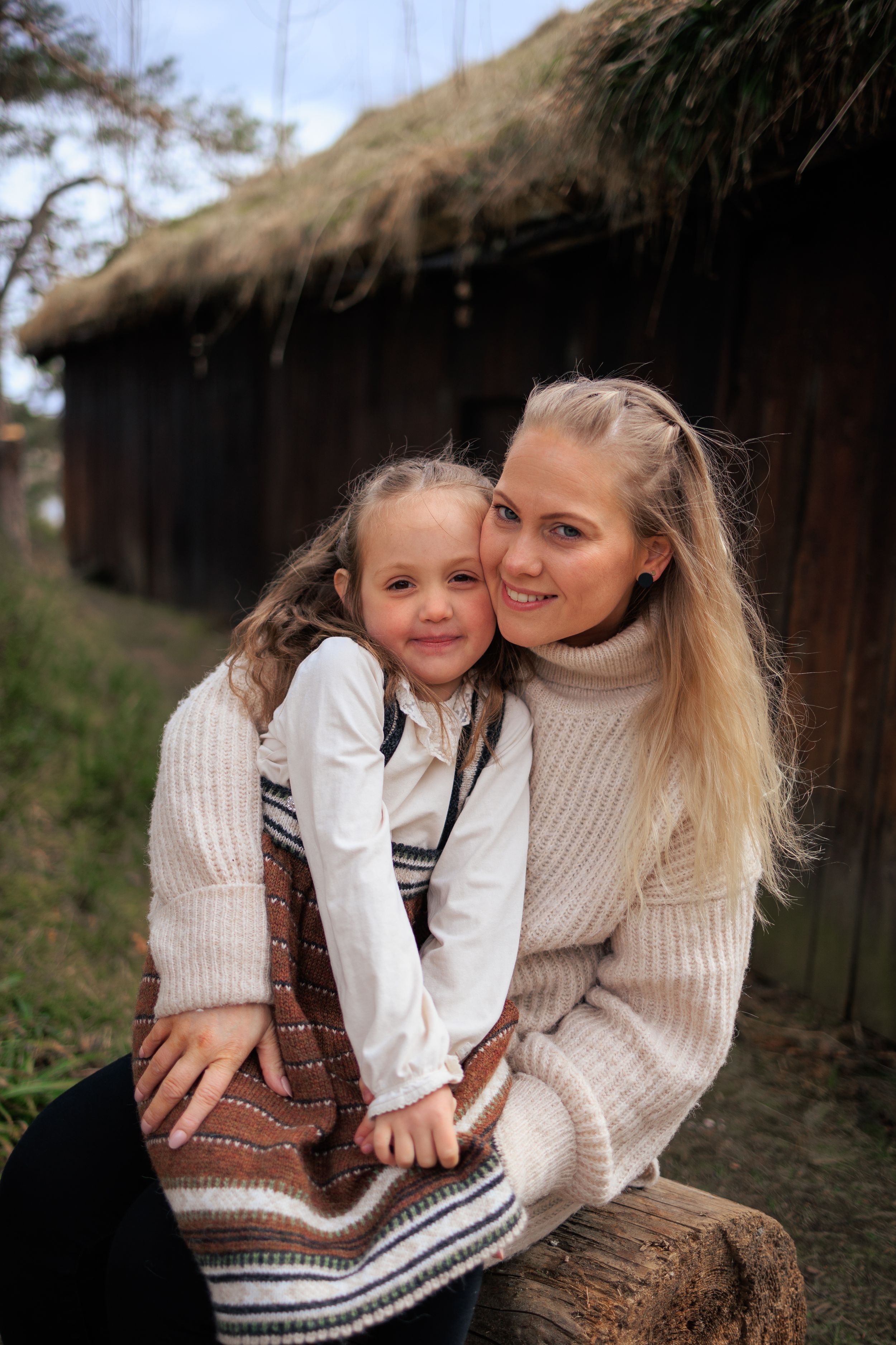 Parent and child in cozy cream sweaters sitting together by rustic barn.