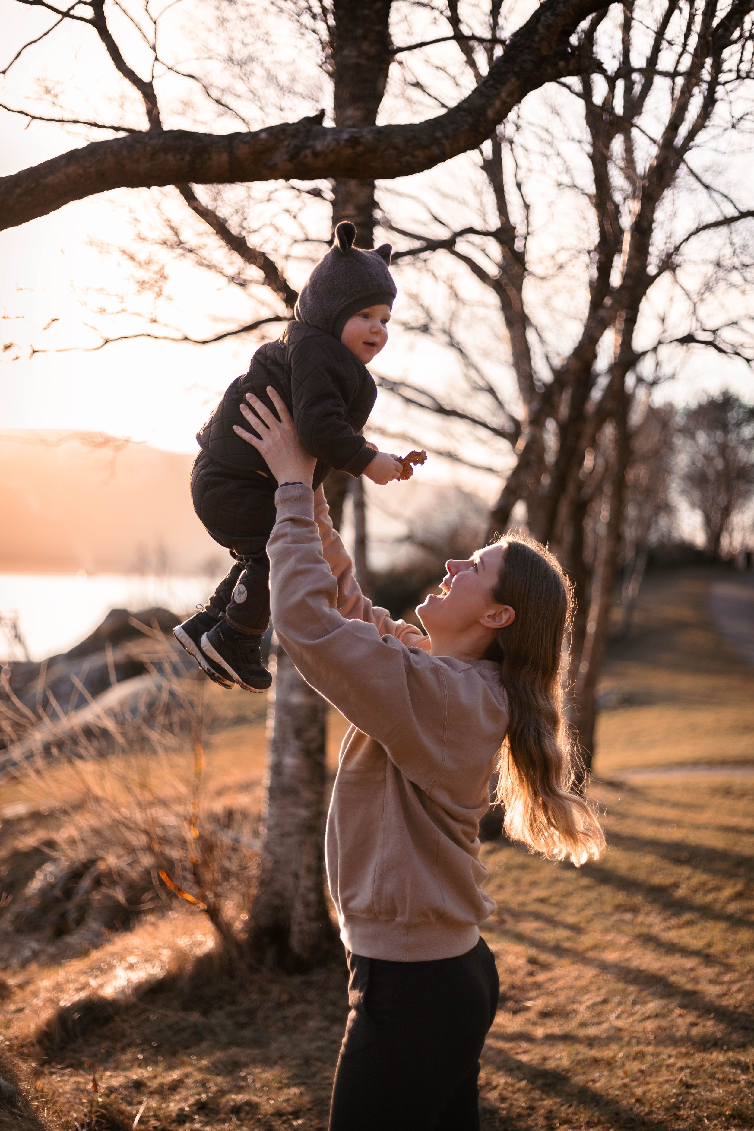 A joyful moment of a parent lifting a small child wearing winter clothes during golden hour.
