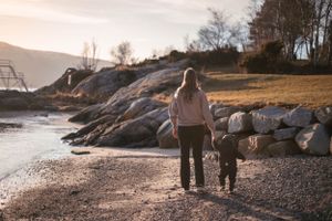 Two people walking along a rocky shoreline during sunset with mountains in the background.