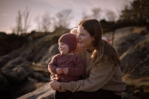 An intimate moment between parent and child sitting on coastal rocks during golden hour.