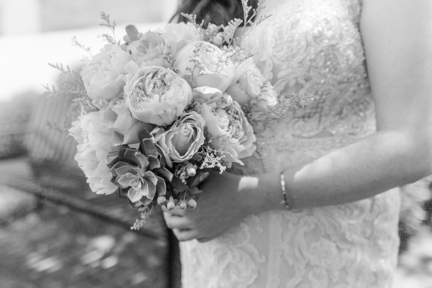 Black and white detail shot of a bridal bouquet with roses and peonies against a lace dress.
