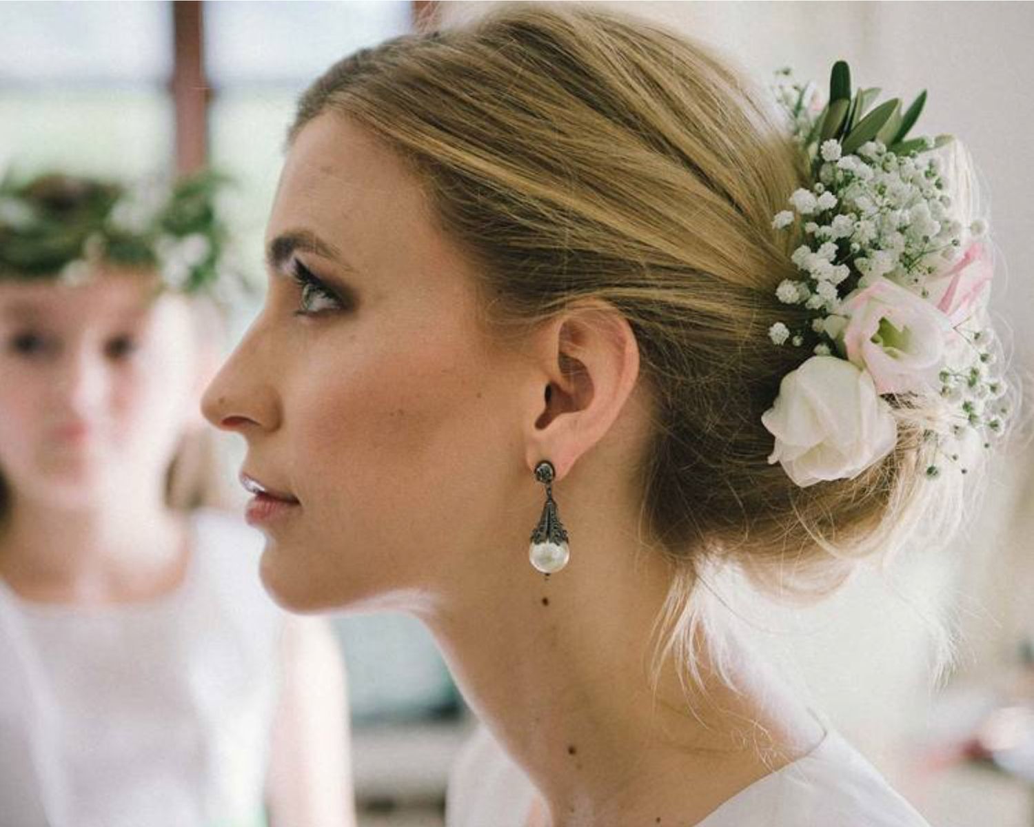 Close-up profile view of an elegant bridal hairstyle with white flowers and dangling earring.