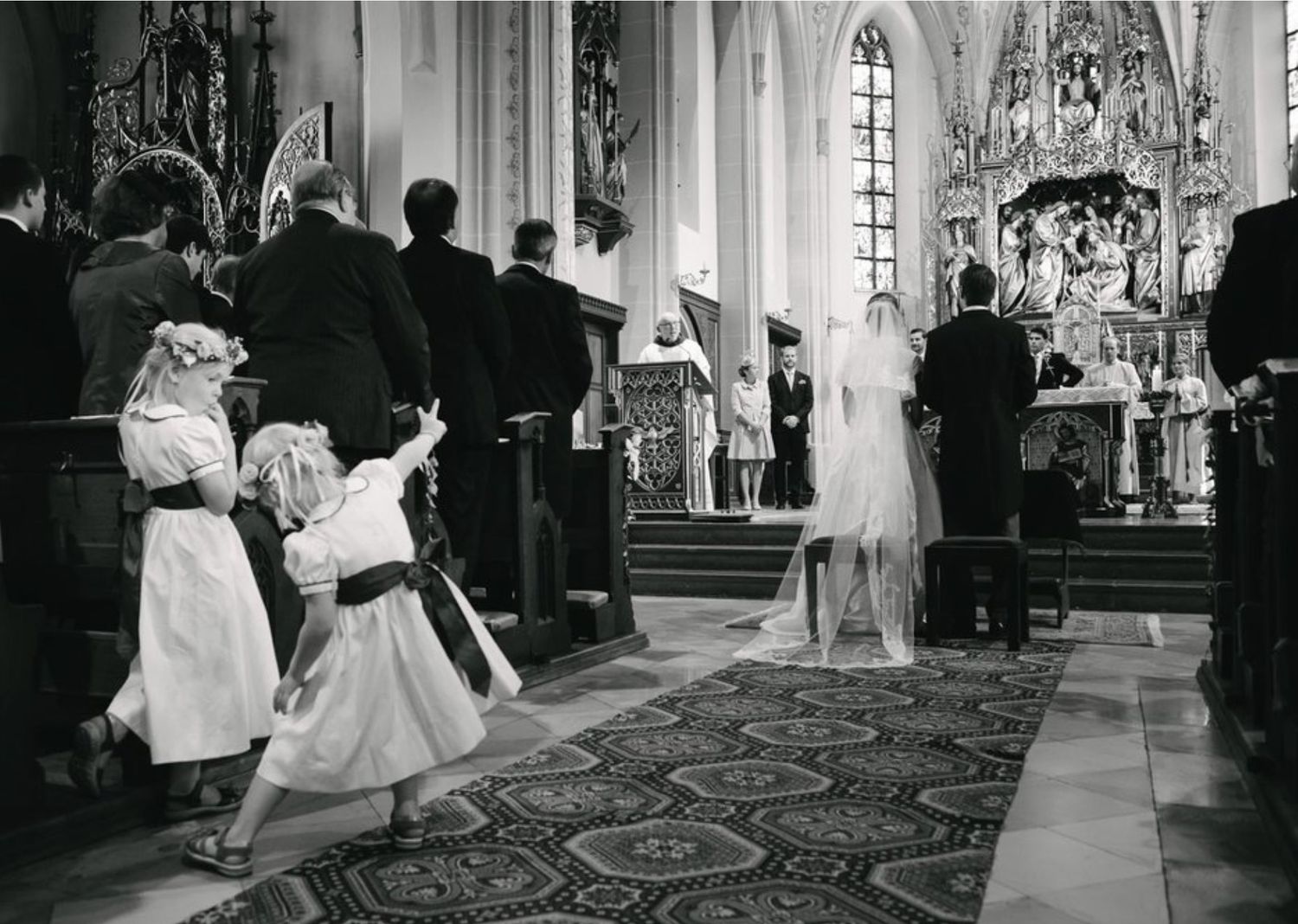 Black and white photo of a traditional church wedding ceremony with children watching from the aisle.