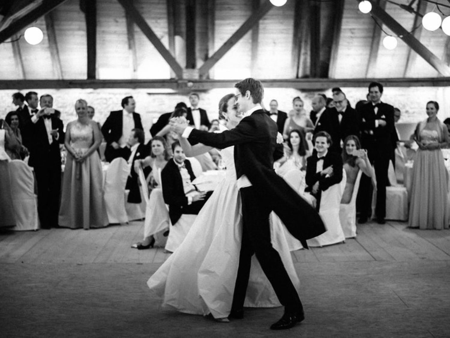 Newlyweds share their first dance surrounded by guests at an elegant reception venue.