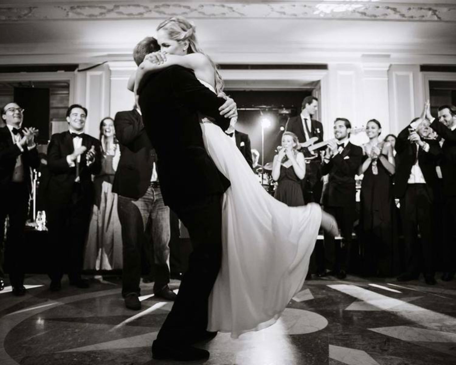 A couple shares an intimate dance moment while guests applaud at their wedding reception.