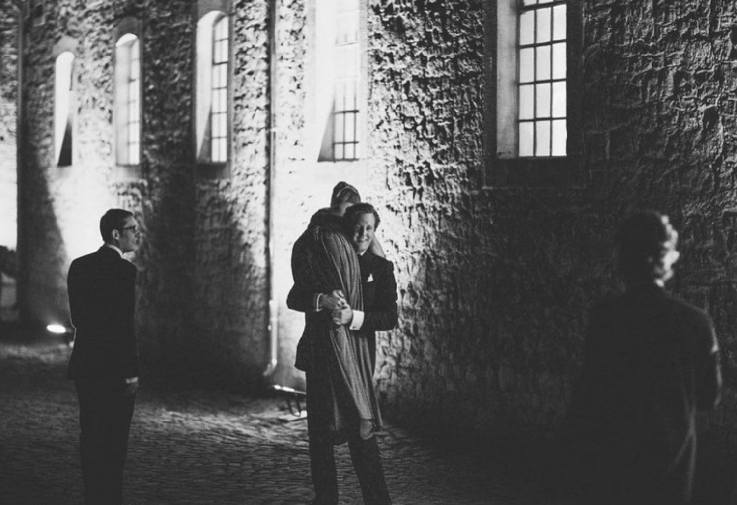 Silhouettes of people standing near an illuminated stone building at night.