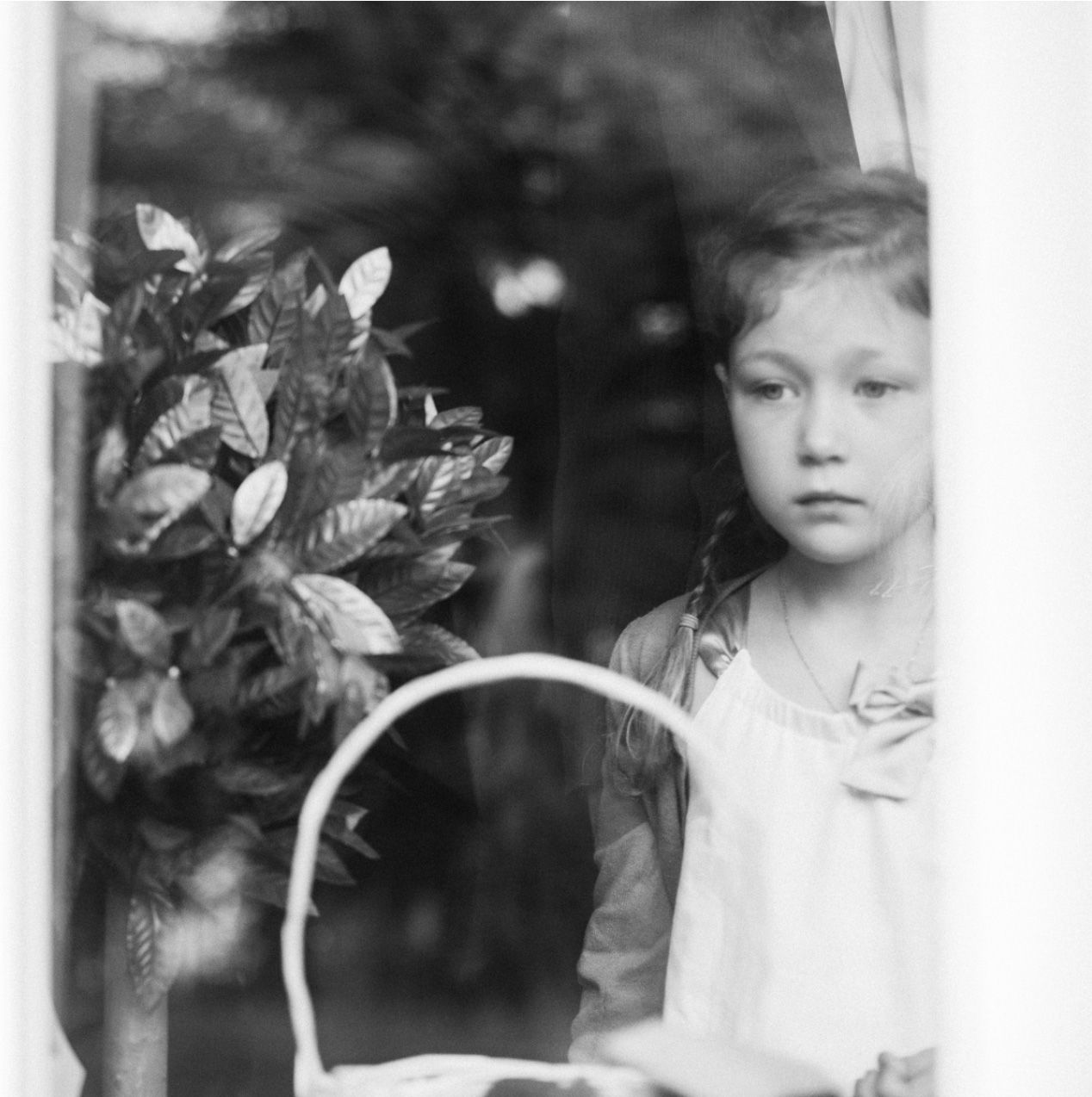 A child stands beside a flower basket in a vintage black and white portrait.