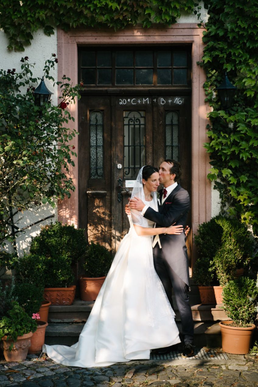 A couple embraces by an ivy-covered doorway in wedding attire.