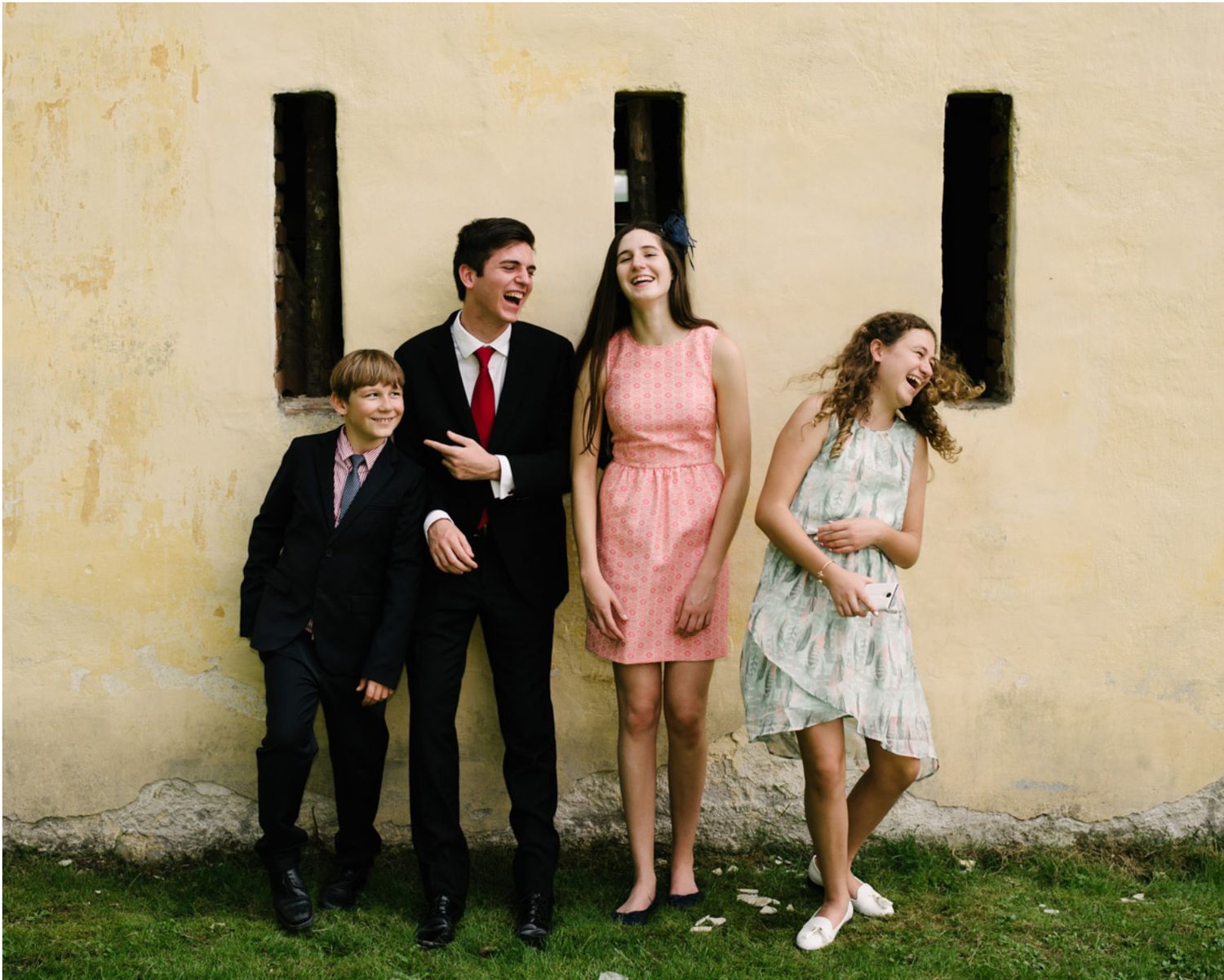 Four people pose against a beige wall wearing coordinated formal attire.