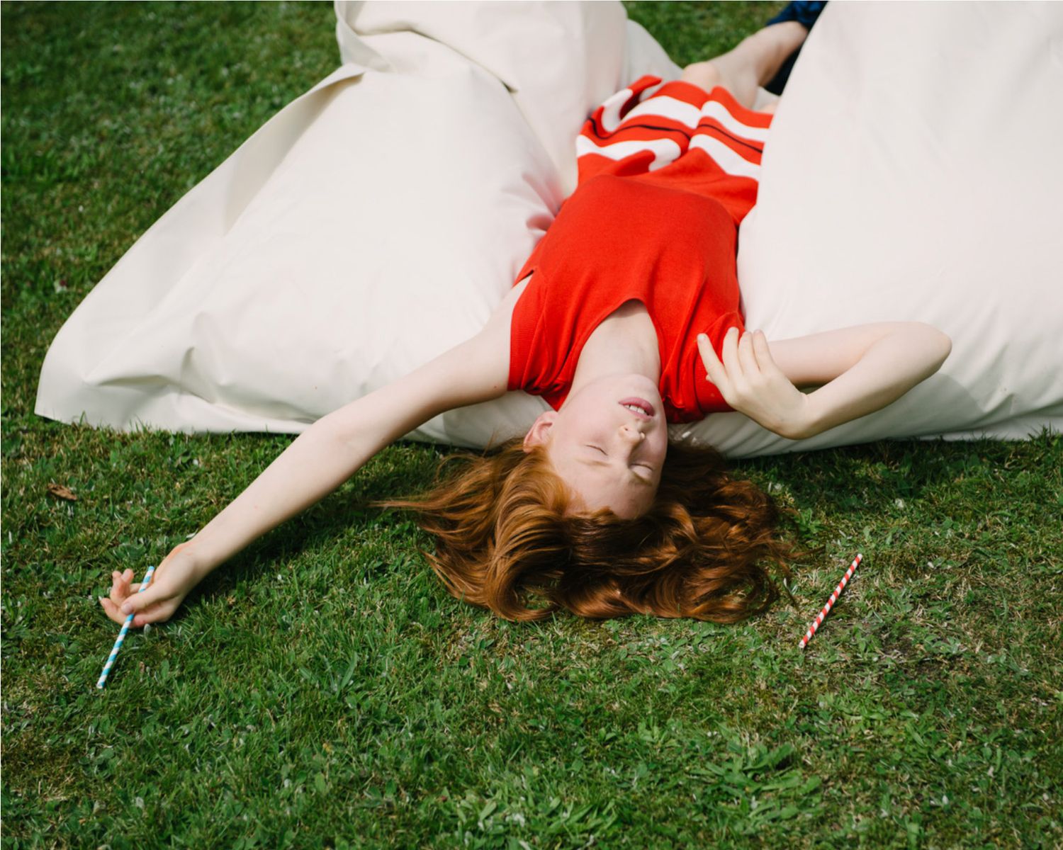 A person in red lies on white blankets in green grass.