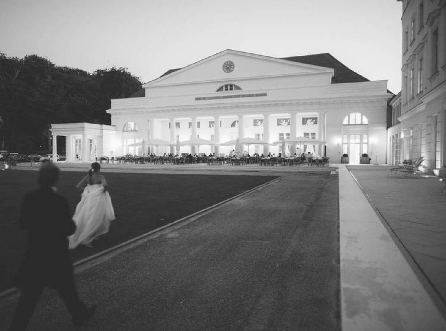 An illuminated classical building facade glows at dusk with figures in the foreground.