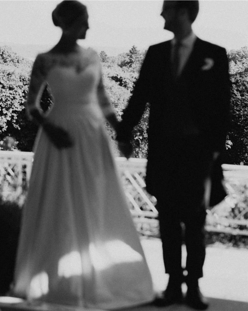 Artistic black and white silhouette of a couple in wedding attire standing outdoors.