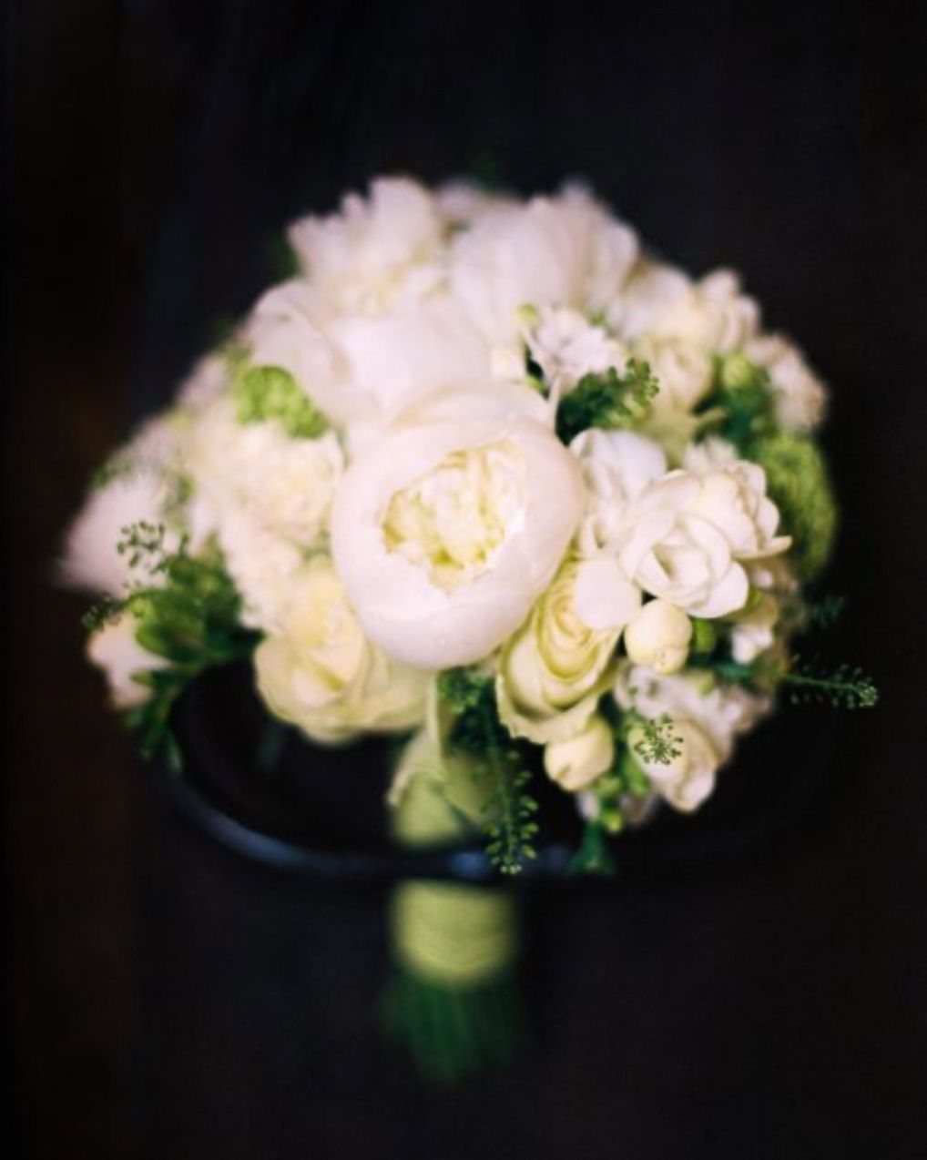 Elegant white and blush pink wedding bouquet with peonies and roses against dark background.