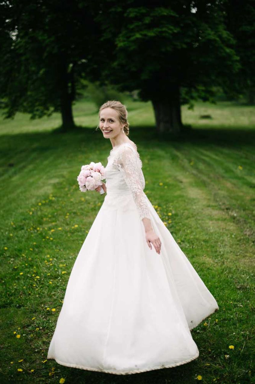 White wedding gown with long sleeves photographed outdoors in a lush green garden setting.