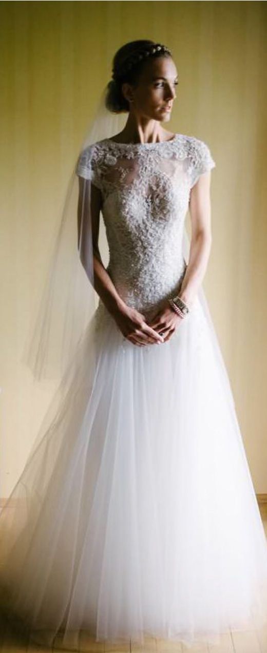 Elegant lace wedding dress with cap sleeves and flowing tulle skirt in soft lighting.