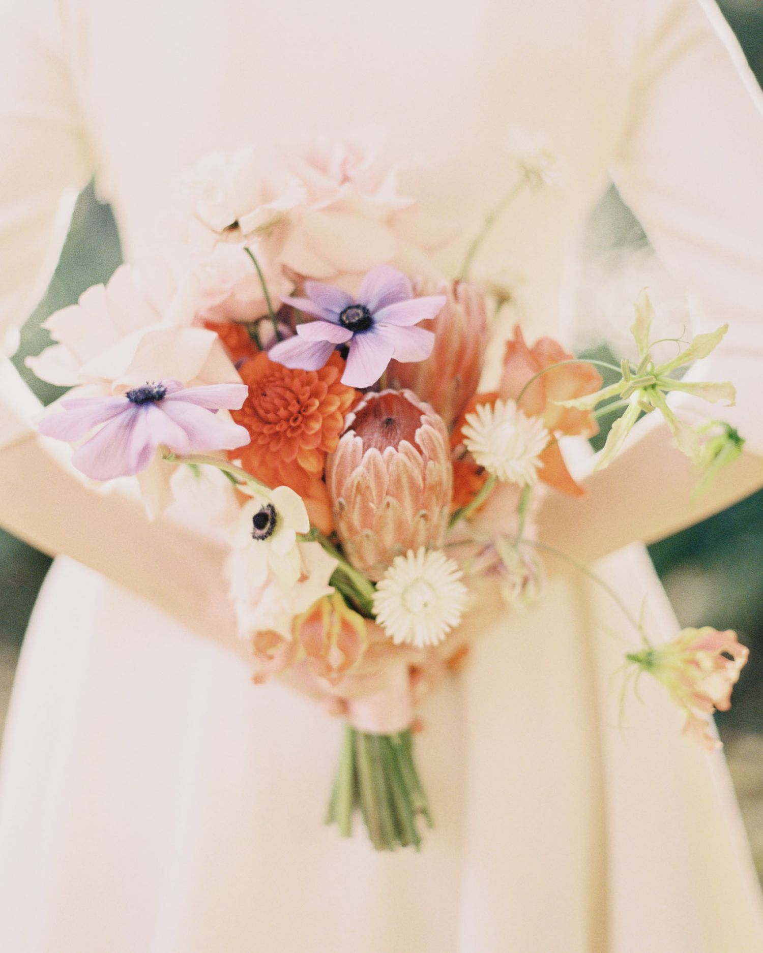 Soft pastel wedding bouquets with anemones and mixed flowers against white fabric.