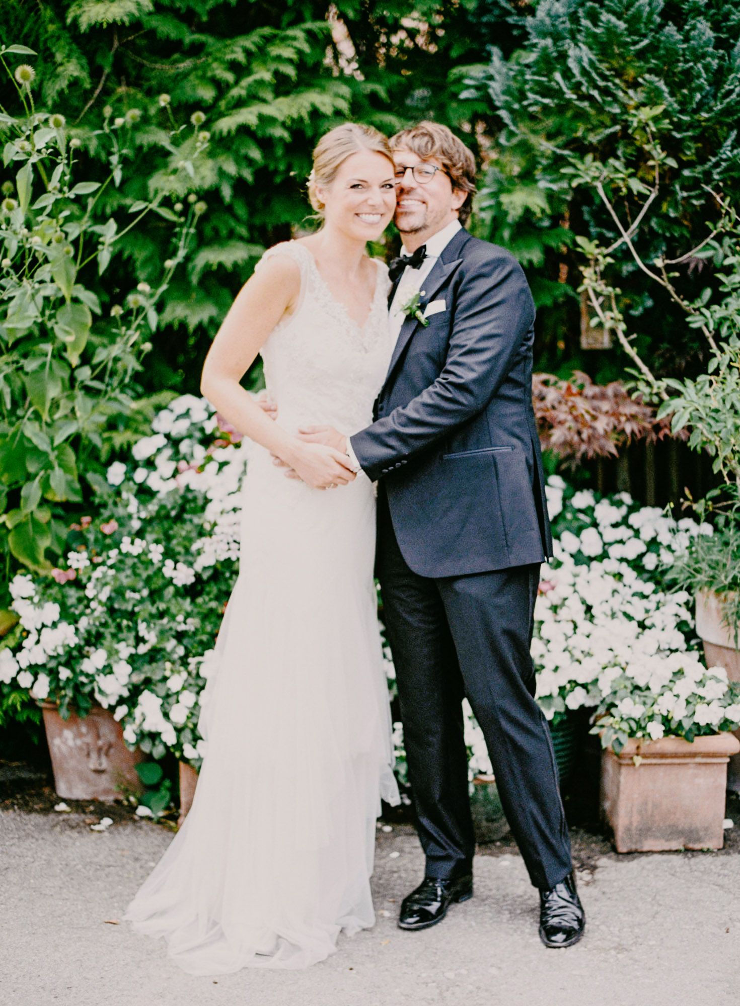 Wedding couple poses in garden setting surrounded by white flowering plants.