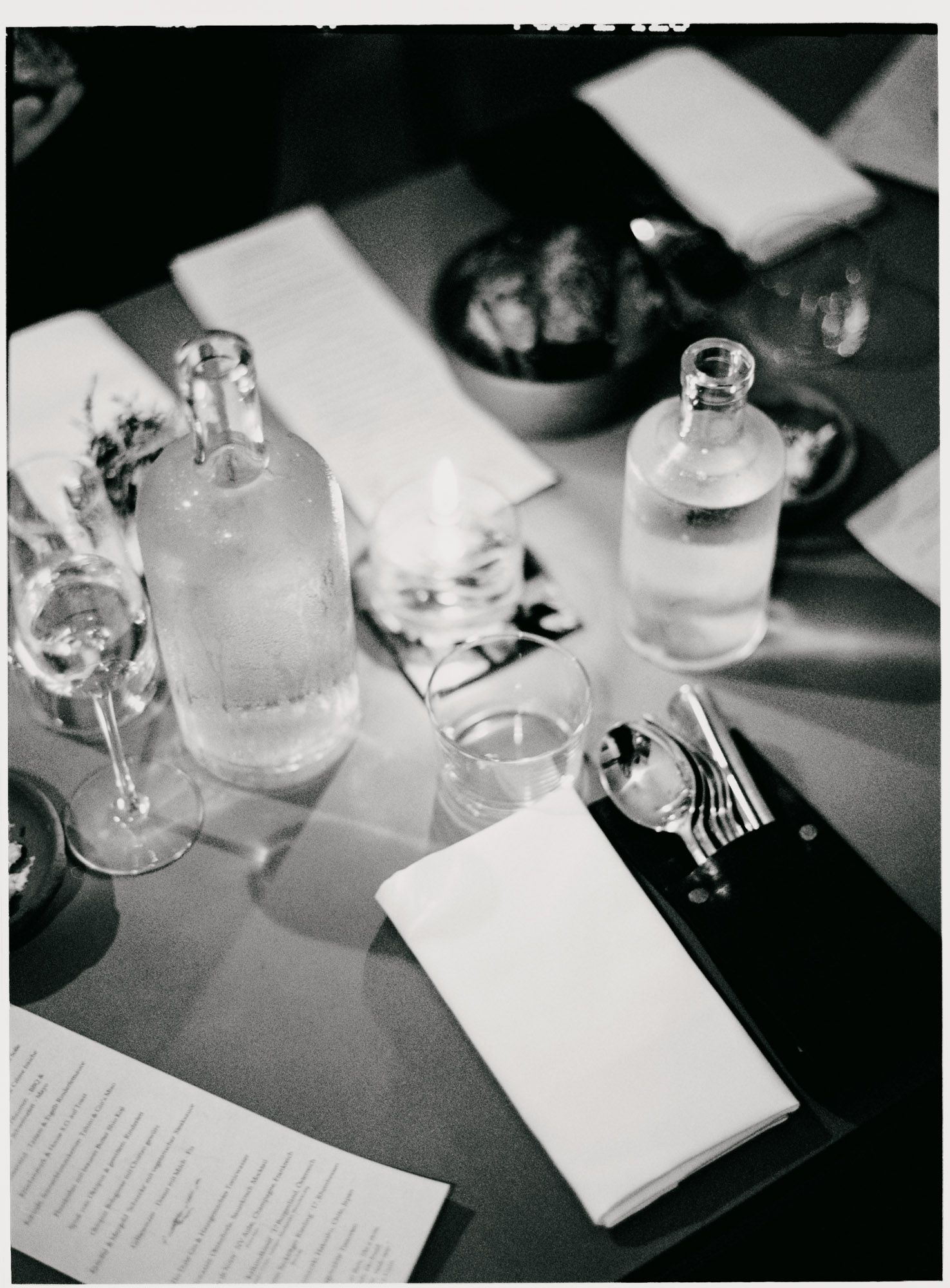 Black and white still life of glass bottles and table settings at a formal dining arrangement.