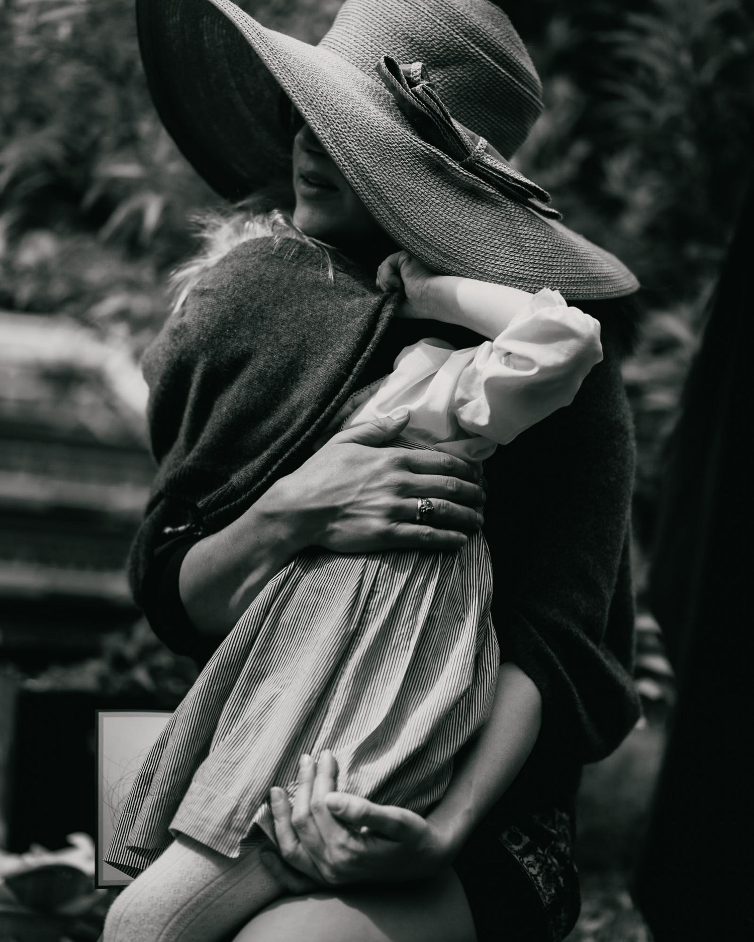 Artistic black and white photograph of an embrace with a wide-brimmed hat creating dramatic shadow.