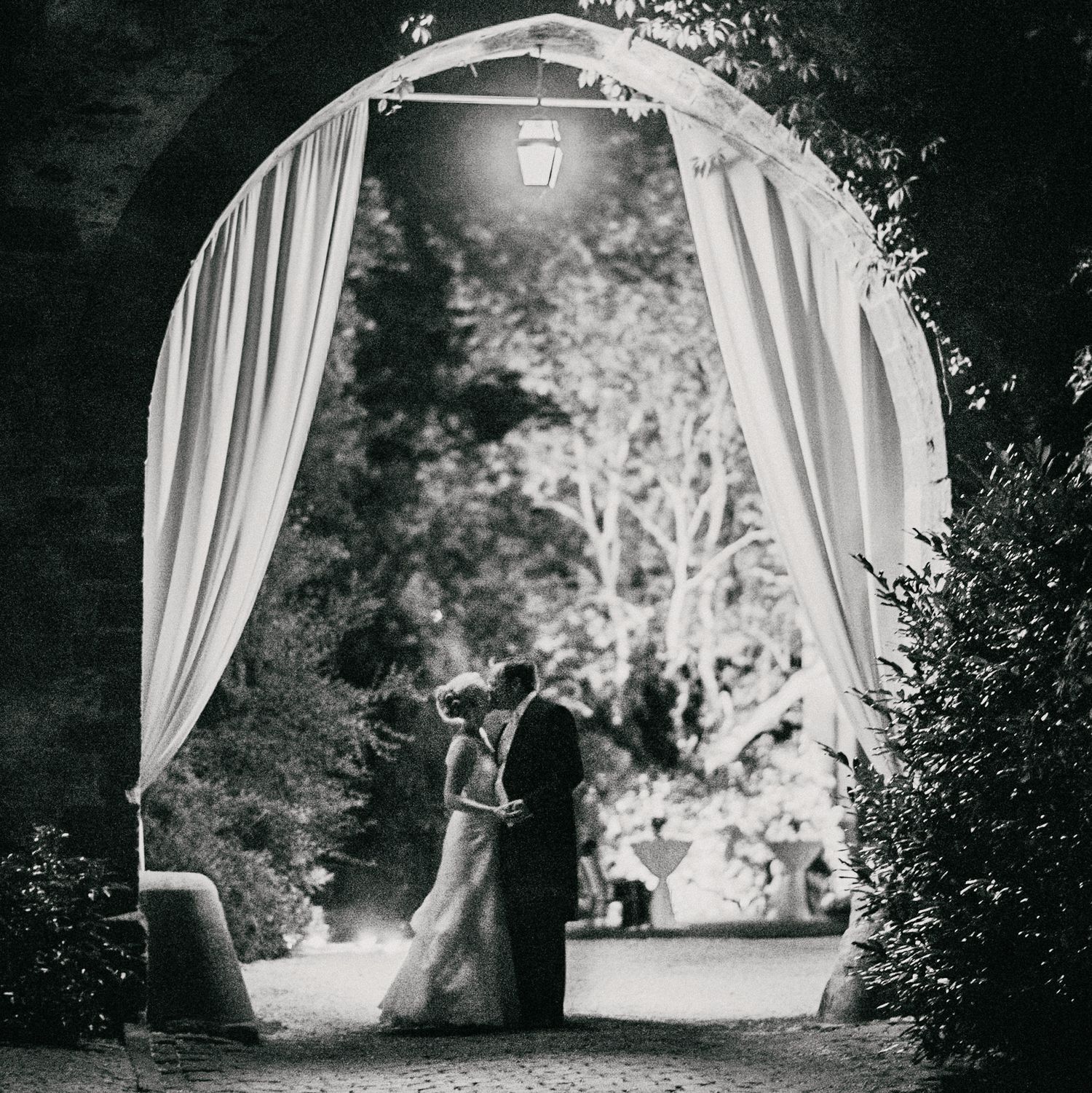 Romantic silhouette of a couple under an illuminated archway with flowing curtains.