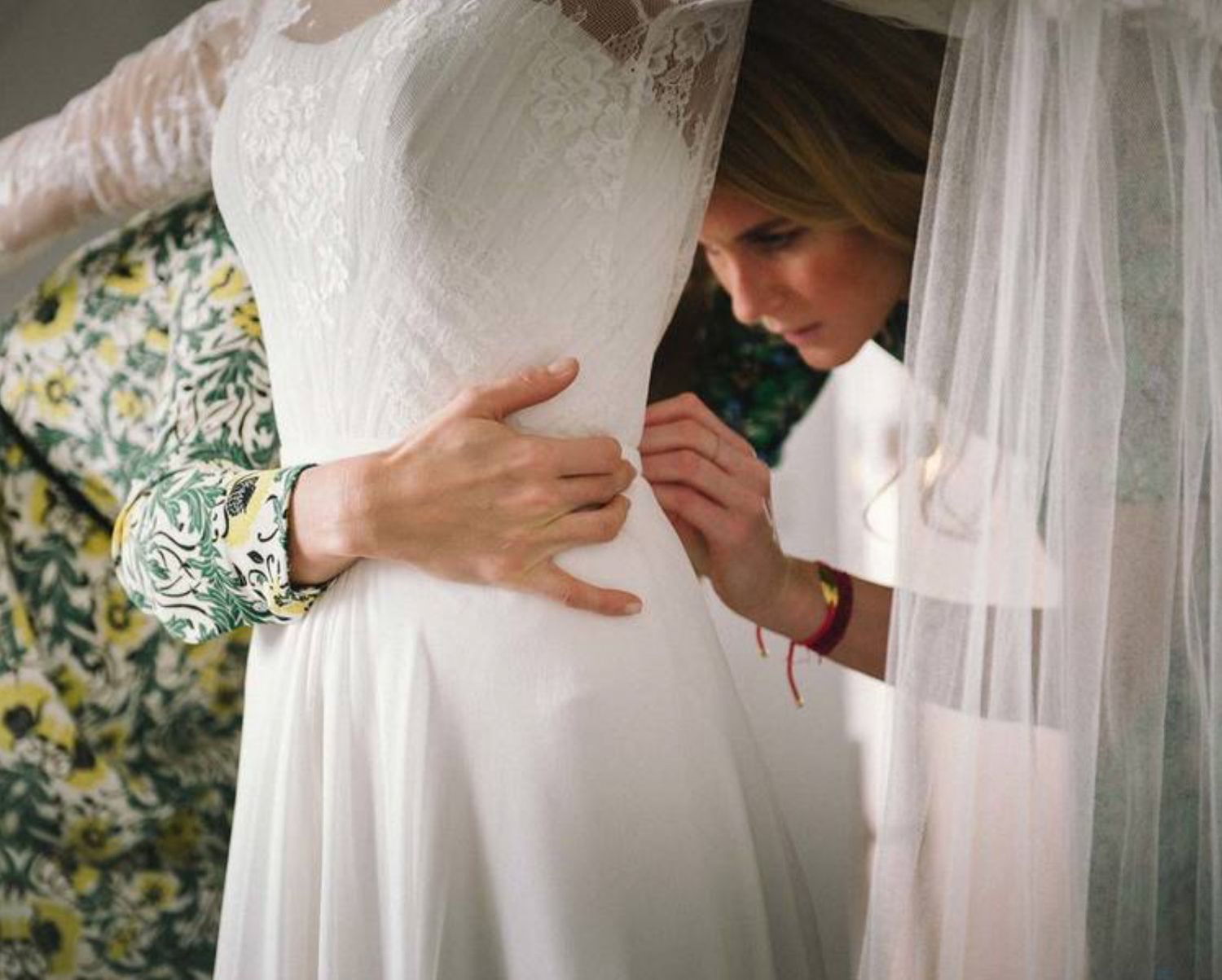 Detail shot of a delicate white lace wedding dress being fitted.