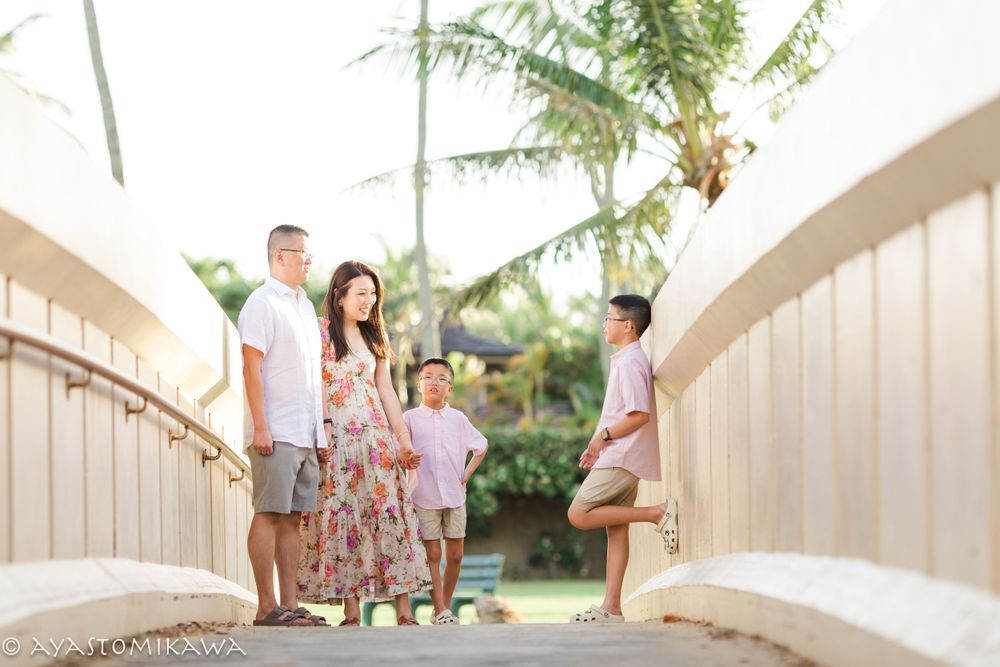 A family stands together on a wooden bridge surrounded by tropical palm trees.
