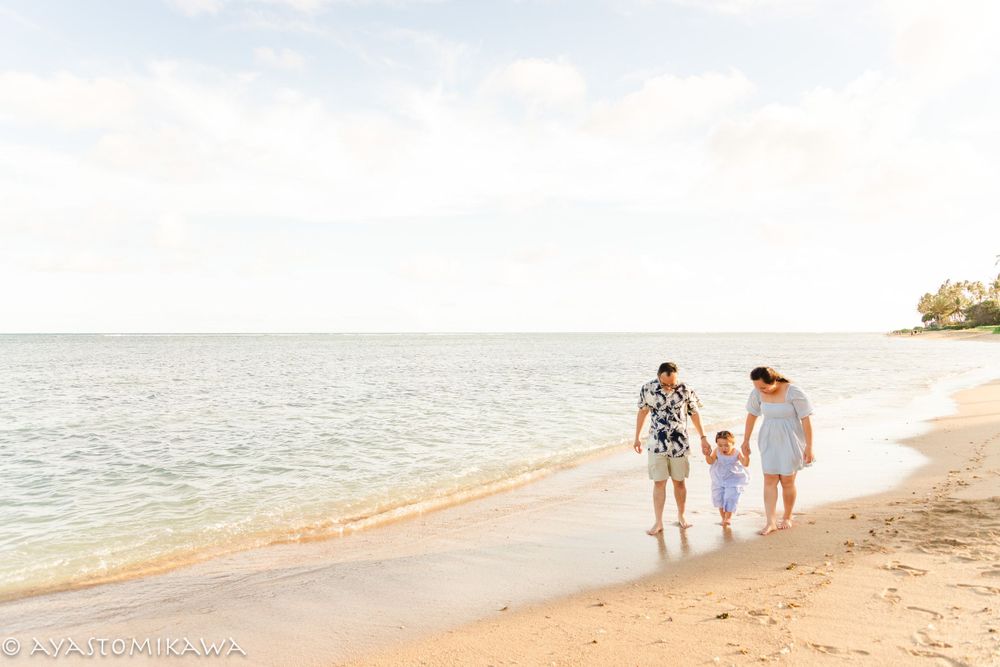 Three people walk along a peaceful beach shoreline during golden hour.
