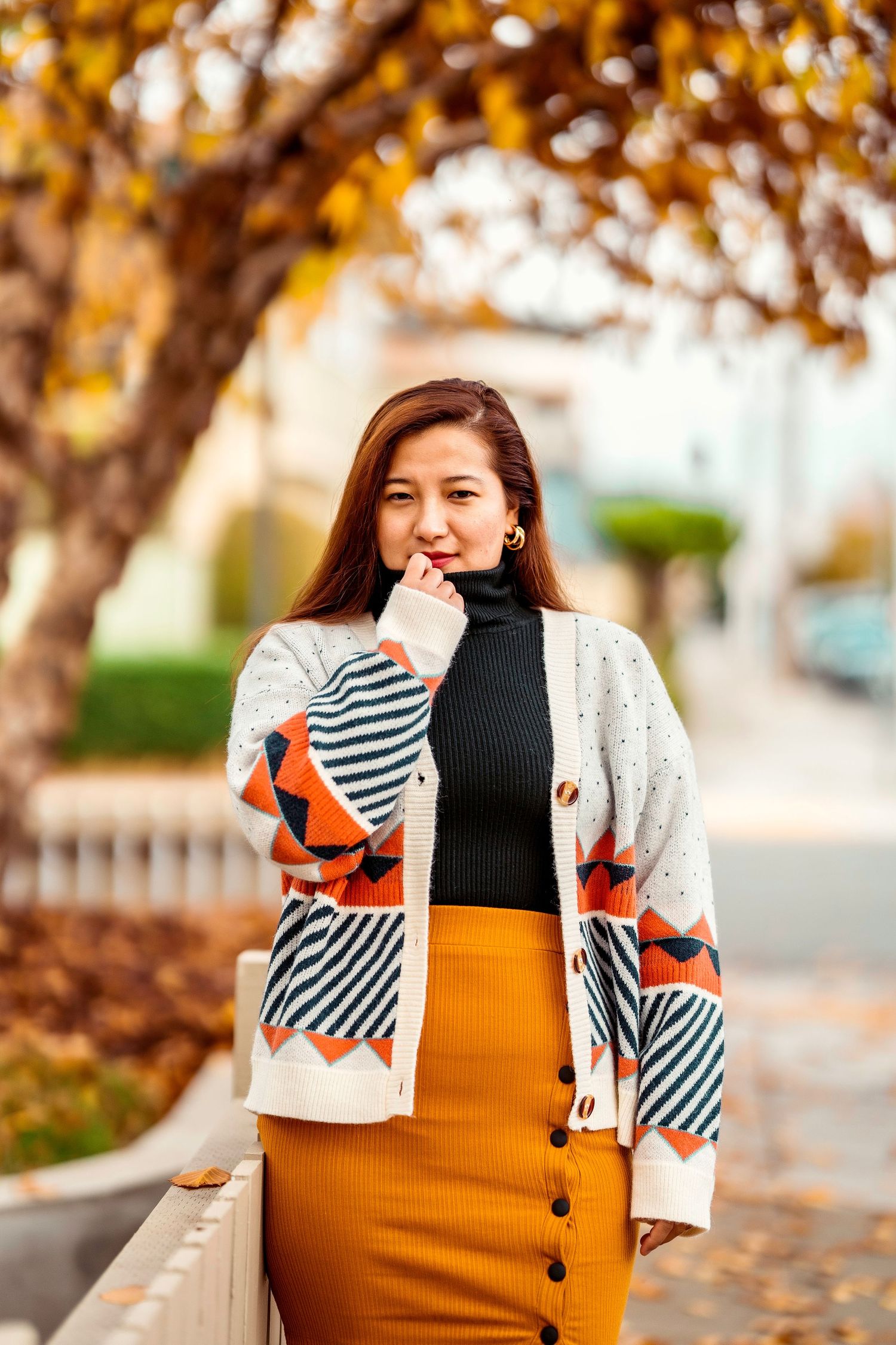 Autumn fashion portrait featuring striped cardigan and mustard skirt against fall foliage.
