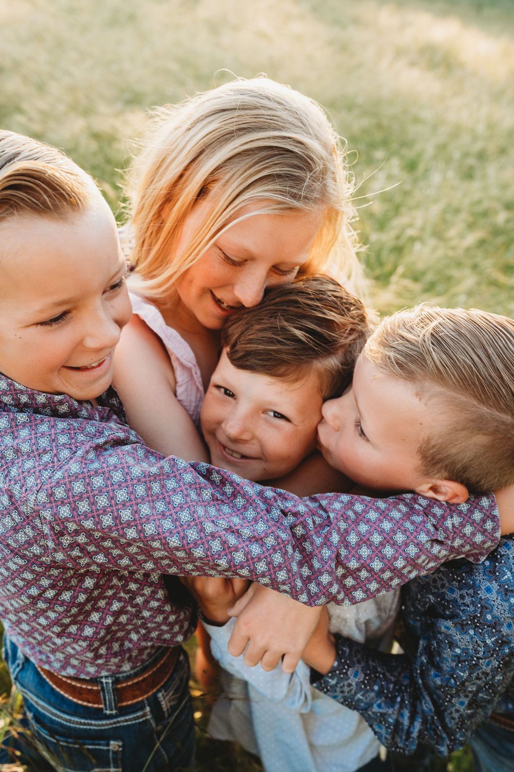 Blonde mother embraced by her three young sons in a warm outdoor group hug.