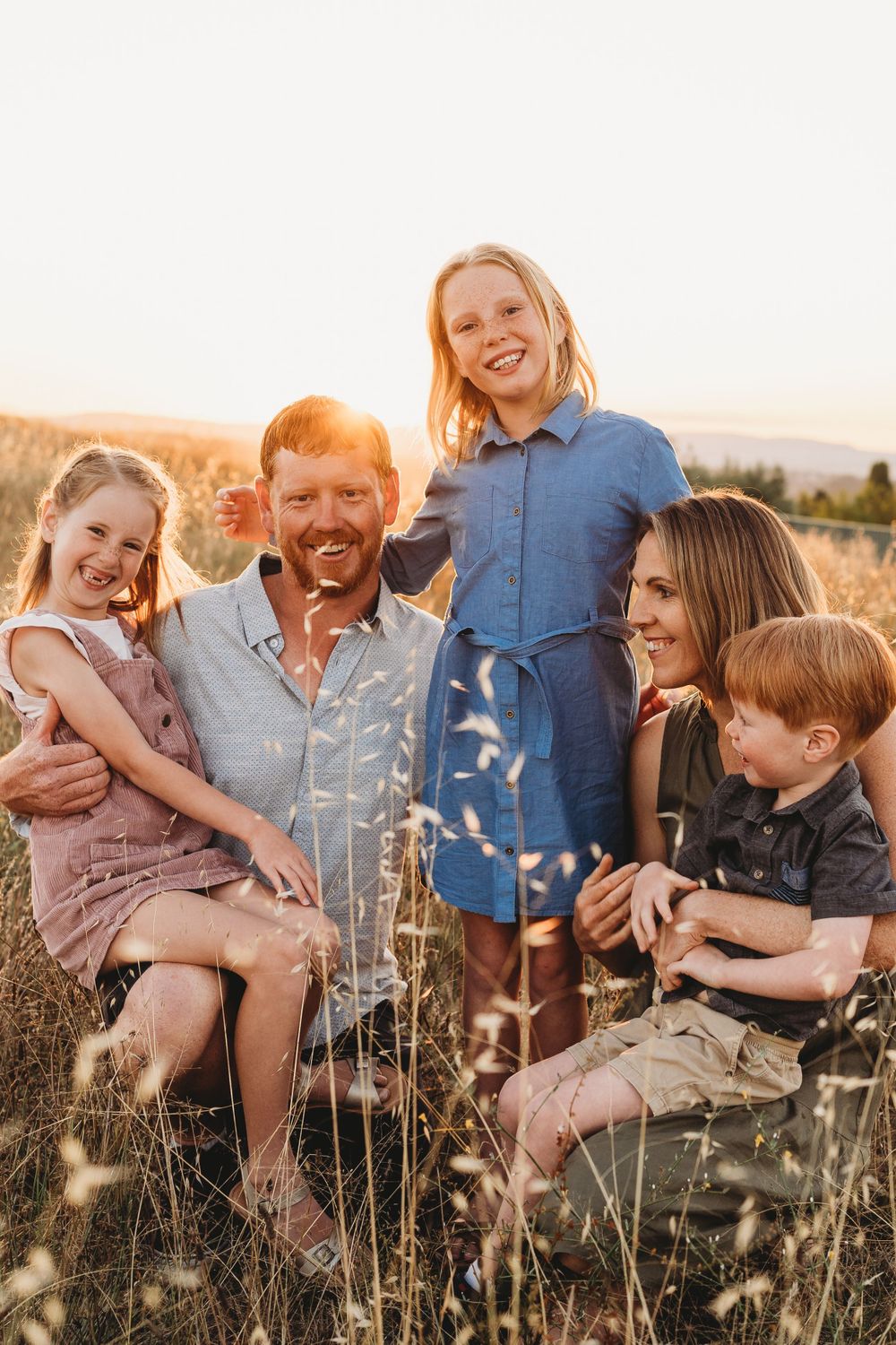 Happy family of five enjoying a golden sunset in a field of tall grass.